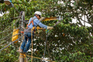 Electrician working on electric pole. Electrician changing, repairing and installing power line on electric pole. Helmet, harness, waist belt and dielectric safety gloves.